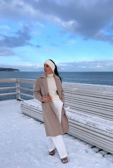 a lady in a white sweater, a grey coat and a pair of white pants